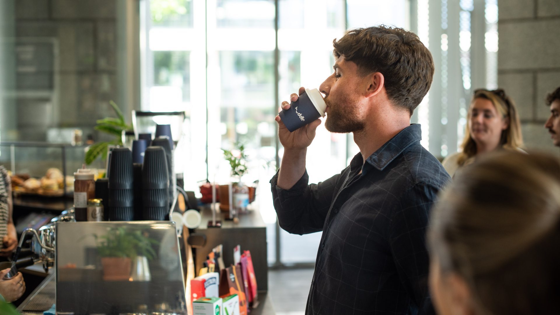 A man drinking coffee from a Huddle branded cup at The Gorilla Cafe in 3 Shortlands, Hammersmith